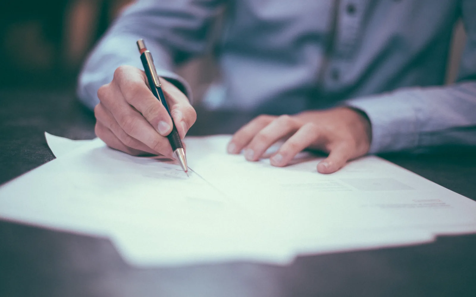 A person signing a paper document with a pen