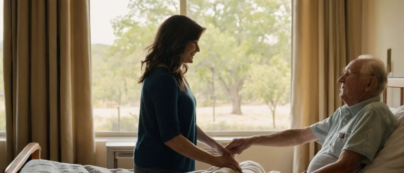 An adult daughter holding her elderly father's hand beside a hospital window in Texas